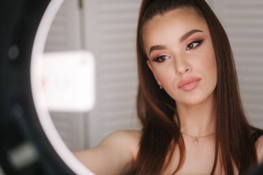 Genç çekici model güzellik stüdyosunda makyaj sonra bir selfie yapmak. Fotoğraf için yüzük lapm kullanıyor. Beyaz katlanır ekranın arka planı