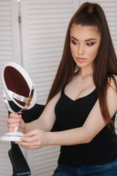 Jong mooi model op zoek in de spiegel na make-up. Aantrekkelijke jonge vrouw zittend in de Beauty Studio. Achtergrond van wit vouwscherm — Stockfoto