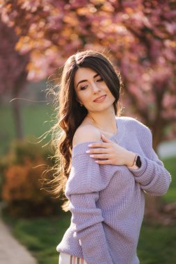 Parktaki sakura ağacının önünde mor bir kazak standında çekici genç kadın