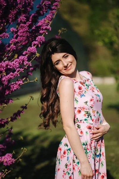 Beautiful woman stand by violet blooming tree. Blue background. Fashion model