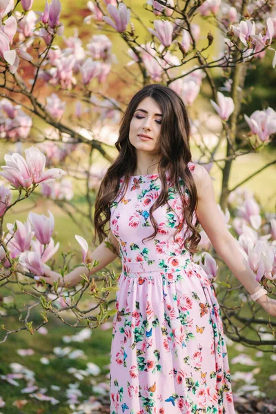 Chica encantadora de pie junto al hermoso árbol de magnolia rosa fuera. Hermosa dama. — Foto de Stock