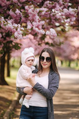 Küçük kızıyla güzel bir anne. Güneş gözlüksi takan annem. Pembe ağacın arka planı