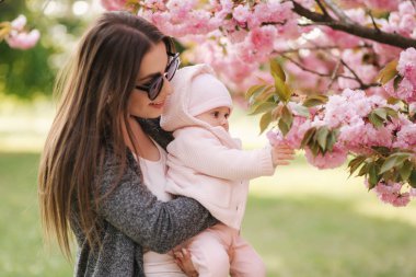 Anne kızı pembe ağaç için zaman firs göster. Mutlu bebek sakura dalı tutun