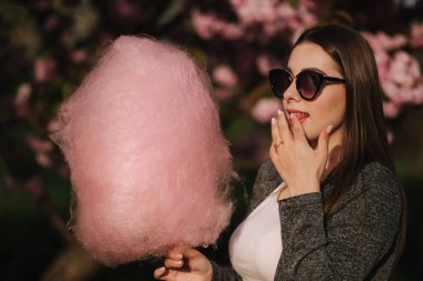 Pembe sakura ağacının önünde pamuk şeker yiyen çekici genç kızın yakın portresi
