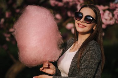 Pembe sakura ağacının önünde pamuk şeker yiyen çekici genç kızın yakın portresi