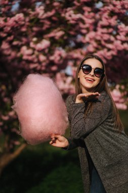 Güzel kahverengi saç modeli elinde bir pamuk şeker tutun ve bir öpücük vermek. Pembe pamuk şeker ile genç kadın