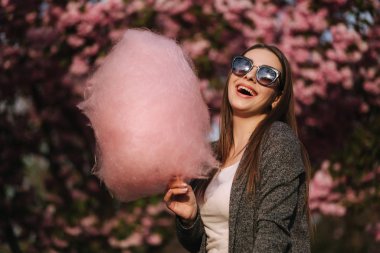 Güzel kahverengi saç modeli elinde bir pamuk şeker tutun ve bir öpücük vermek. Pembe pamuk şeker ile genç kadın