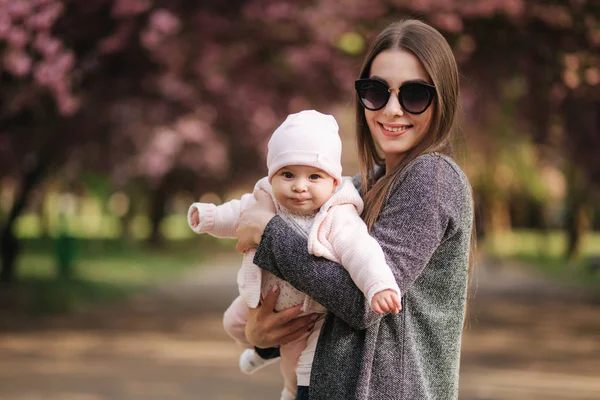 Portrait of mother and her little baby girl. Beautiful mom and cute baby. Mother hud her daughter. Baby dressed in peanch colour hat and smile — Stock Photo, Image