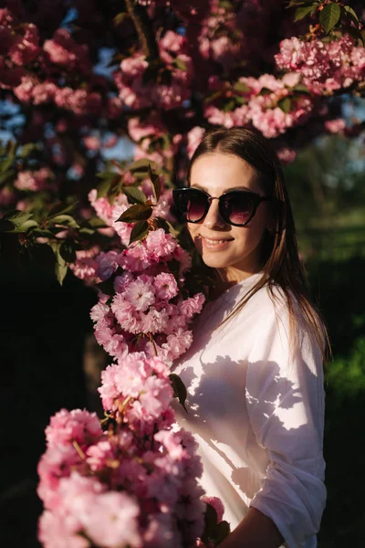 Schöne Frau mit Sonnenbrille steht im Sakura-Baum — Stockfoto