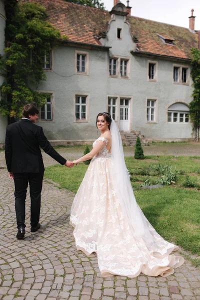 Yeni evliler büyük kalenin yanındaki parkta yürüyorlar. Yakışıklı damat ile güzel gelin — Stok fotoğraf