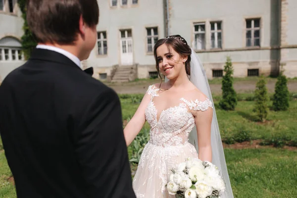 Newlyweds are walking in the park near the big castle. Beautiful bride with handsome groom — Stock Photo, Image