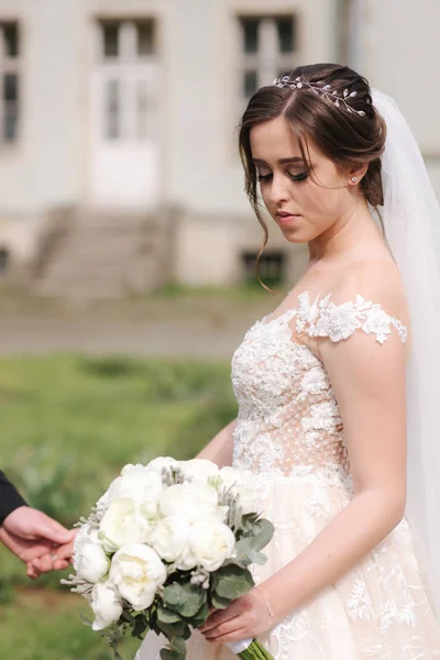 Newlyweds are walking in the park near the big castle. Beautiful bride with handsome groom — Stock Photo, Image