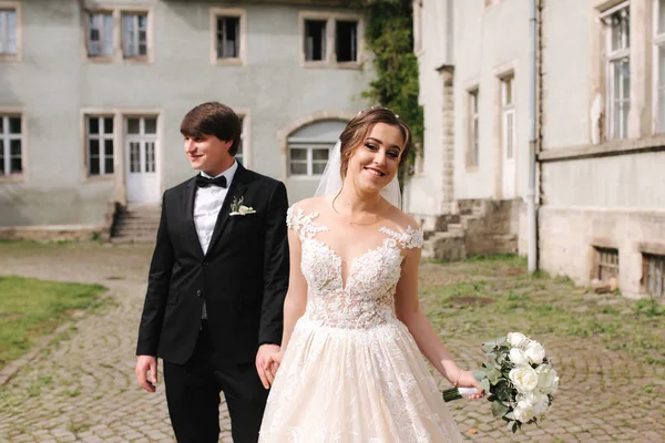 Felice coppia appena sposata in abiti da sposa a piedi vicino al castello — Foto Stock
