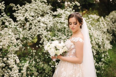 Muhteşem gelinlik Büyüleyici gelin tutun buket ve çiçek açan ağaçların önünde durmak