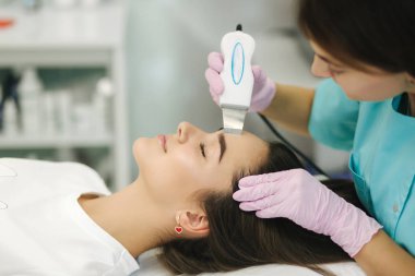 Yumuşak tenli bir kadın yüzü. Kozmetoloji kliniğindeki kadın cilde yapışmak için güzellik prosedürü uyguluyor.