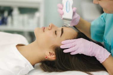 Yumuşak tenli bir kadın yüzü. Kozmetoloji kliniğindeki kadın cilde yapışmak için güzellik prosedürü uyguluyor.