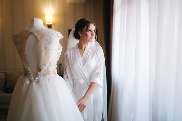 Jeune et belle mariée stand par sa robe de mariée — Photo