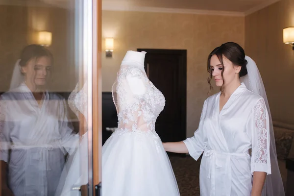 Jeune et belle mariée stand par sa robe de mariée — Photo
