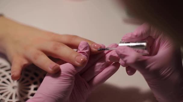 O close-up de mulheres pinta pregos. Arte de unhas de manicure. A fêmea trabalha com luvas cor de rosa. Fechar as mãos de mulheres — Vídeo de Stock