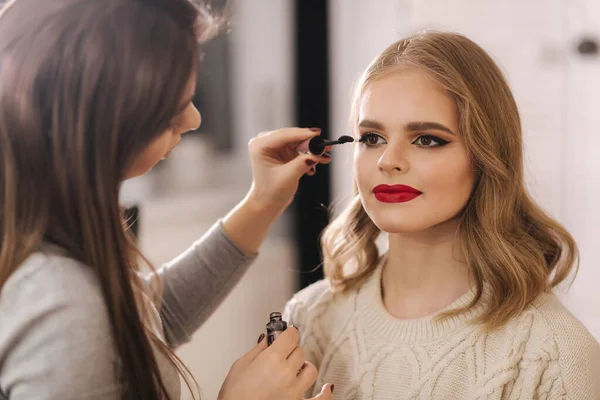 Truccatore lavoro in studio di bellezza. Donna che si applica da professionista make up master. Bella make up artist fare un trucco per modello di capelli biondi — Foto Stock