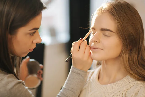 Makeup artist lavora nel suo studio di bellezza. Ritratto di donna che applica da maestro professionista di trucco. Bella make up artist iniziare a fare un trucco per modello di capelli biondi — Foto Stock