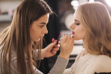 Makyöz güzellik stüdyosunda çalışıyor. Profesyonel makyaj ustası tarafından başvurulan kadın. Güzel makyöz, sarı saç modeline makyaj yapar.