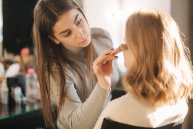 Makyöz güzellik stüdyosunda modelle çalışır. Çalışmaya başla. Makyajsız model. Güzel makyaj sanatçısı.