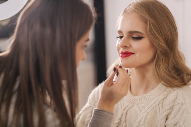 Makyöz güzellik stüdyosunda çalışıyor. Profesyonel makyaj ustası tarafından başvurulan kadın. Güzel makyöz, sarı saç modeline makyaj yapar.