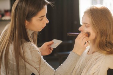 Makyöz güzellik stüdyosunda modelle çalışır. Çalışmaya başla. Makyajsız model. Güzel makyaj sanatçısı.