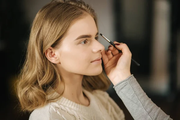 Makeup artist work in her beauty studio. Portrait of Woman applying by professional make up master. Beautiful make up artist start making a makeup for blond hair model