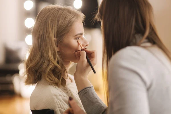 Makeup artist work in her beauty studio. Portrait of Woman applying by professional make up master. Beautiful make up artist start making a makeup for blond hair model — Stock Photo, Image