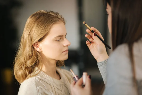 Maskenbildnerin arbeitet in ihrem Schönheitsstudio. Porträt einer Frau, die sich mit einem professionellen Make-up-Meister bewirbt. Schöne Make-up-Artist beginnen, ein Make-up für blonde Haare Modell — Stockfoto