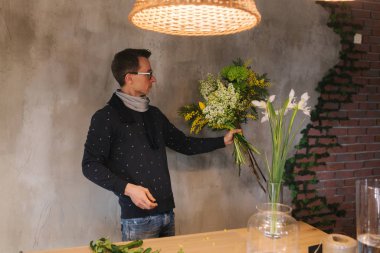 Erkek, bahar buketi yapar. Çiçekçideki bahçıvanlar buket yaparlar. Hayat tarzı çiçek dükkanı. Sarı çiçeklerin güzel kompozisyonu