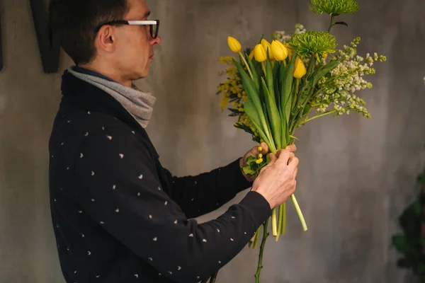 Tienda de entrega de flores. Florista creando orden, haciendo ramo de primavera. Macho hacer ramo usando tulipanes amarillos y lila —  Fotos de Stock