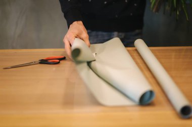 Erkek, bahar buketi yapar. Çiçekçi adam, güzel bir demet bahar çiçeğini ahşap masaya ambalaj kağıdıyla sarıyordu. Sarı çiçeklerin güzel kompozisyonu