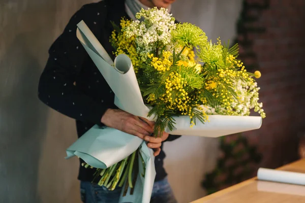 Macho hacer ramo de primavera. Hombre florista envolviendo hermoso ramo de flores de primavera en papel de paquete en la mesa de madera. Hermosa composición de flores amarillas —  Fotos de Stock