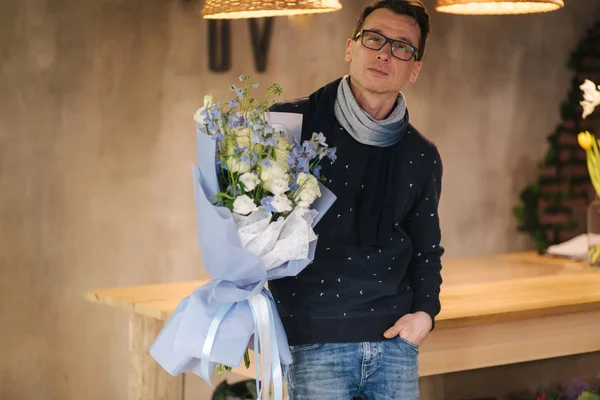 Homme élégant dans des lunettes tenir bouquet de fleurs à l'extérieur. Contexte du mur de briques — Photo