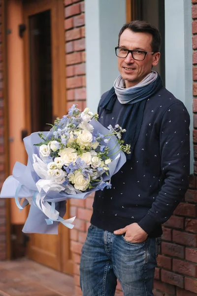 안경을 쓴 품위있는 남자 가 밖에 꽃다발을 들고 있다. 벽돌 벽의 배경 — 스톡 사진