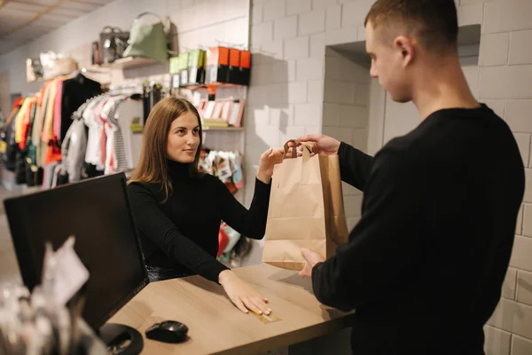 Çekici bir kadın mağaza müdürüne kredi kartı veriyor. Müşteri yardımcısına kredi kartı verir ve butikte alışveriş yaparken gülümser. — Stok fotoğraf