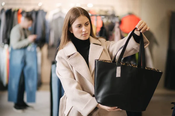 Young woman trying on black bag. Woman in boutique