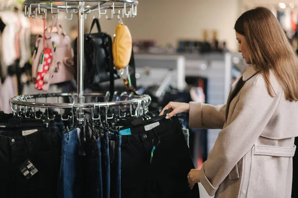 Jonge mooie vrouw op zoek naar nieuwe jeans in kleding winkel — Stockfoto