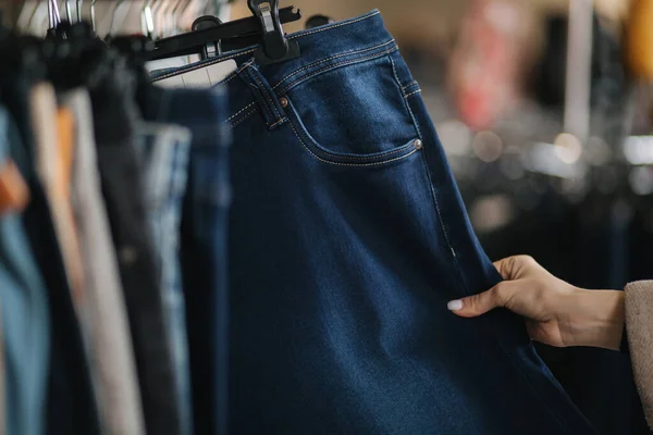 女性选择牛仔裤的特写镜头。女店员在服装店手握牛仔裤 — 图库照片