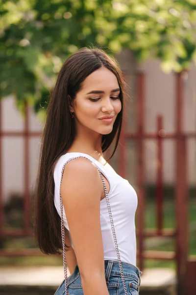 Aantrekkelijke jonge vrouw wandelen in de stad in de zomer. Mooie brunette in wit shirt. Glimlach — Stockfoto