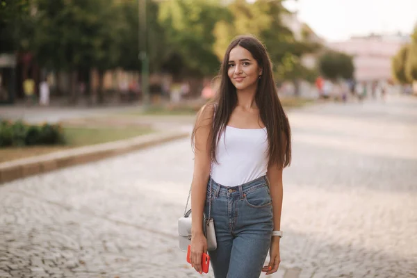 Atraktivní mladá žena procházky v centru města v letním čase. Krásná brunetka v bílé košili. Úsměv — Stock fotografie