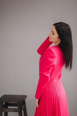 Kırmızı elbiseli çekici esmer model. Stüdyoda gri arka planda.