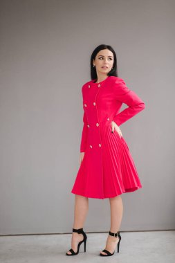 Kırmızı elbiseli çekici esmer model. Stüdyoda gri arka planda.