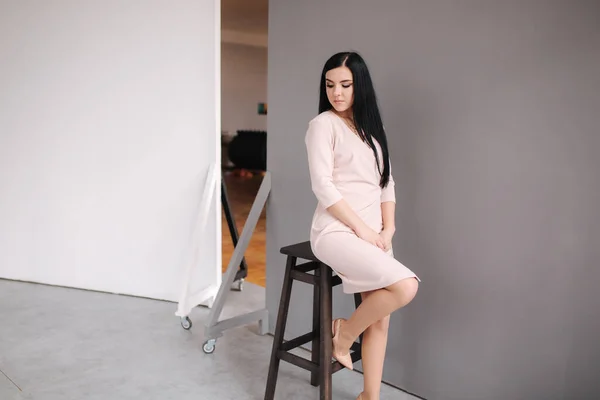 Елегантна брюнетка в стильній сукні позує в студії на сірому фоні — стокове фото
