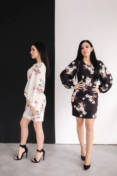 Två modebrunettmodeller i vårklänningar som poserar i ateljén. Svart och vit bakgrund — Stockfoto