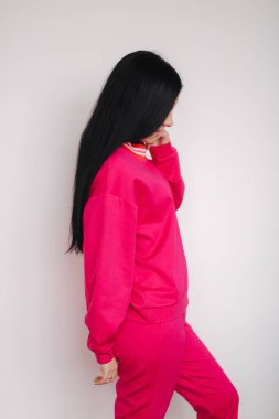 Pembe eşofmanlı çekici genç bir manken. Stüdyoda kıyafet sergileyen bir kadın. Beyaz arkaplan