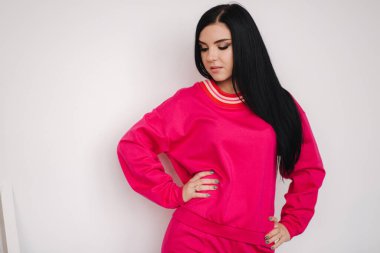 Pembe eşofmanlı çekici genç bir manken. Stüdyoda kıyafet sergileyen bir kadın. Beyaz arkaplan